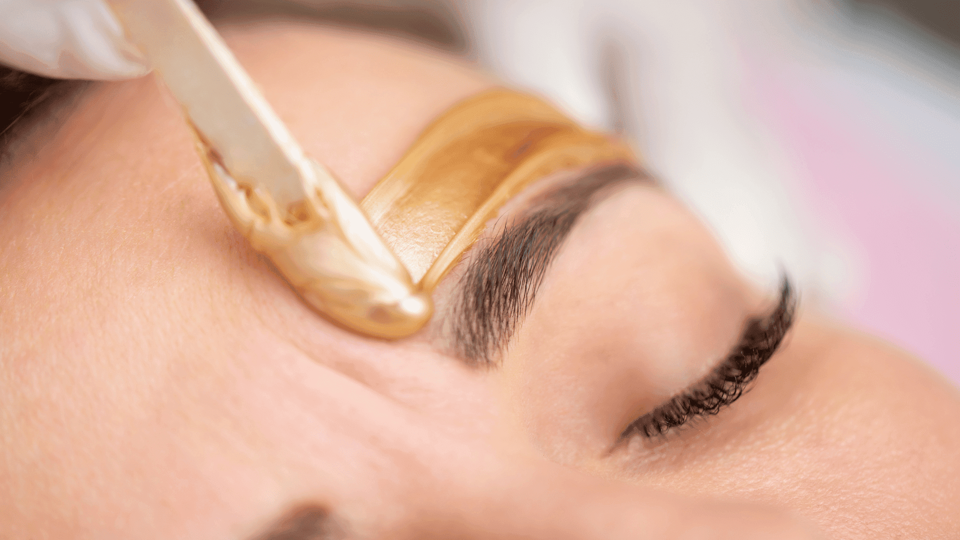 Applying warm wax on an eyebrow for shaping at a beauty salon.