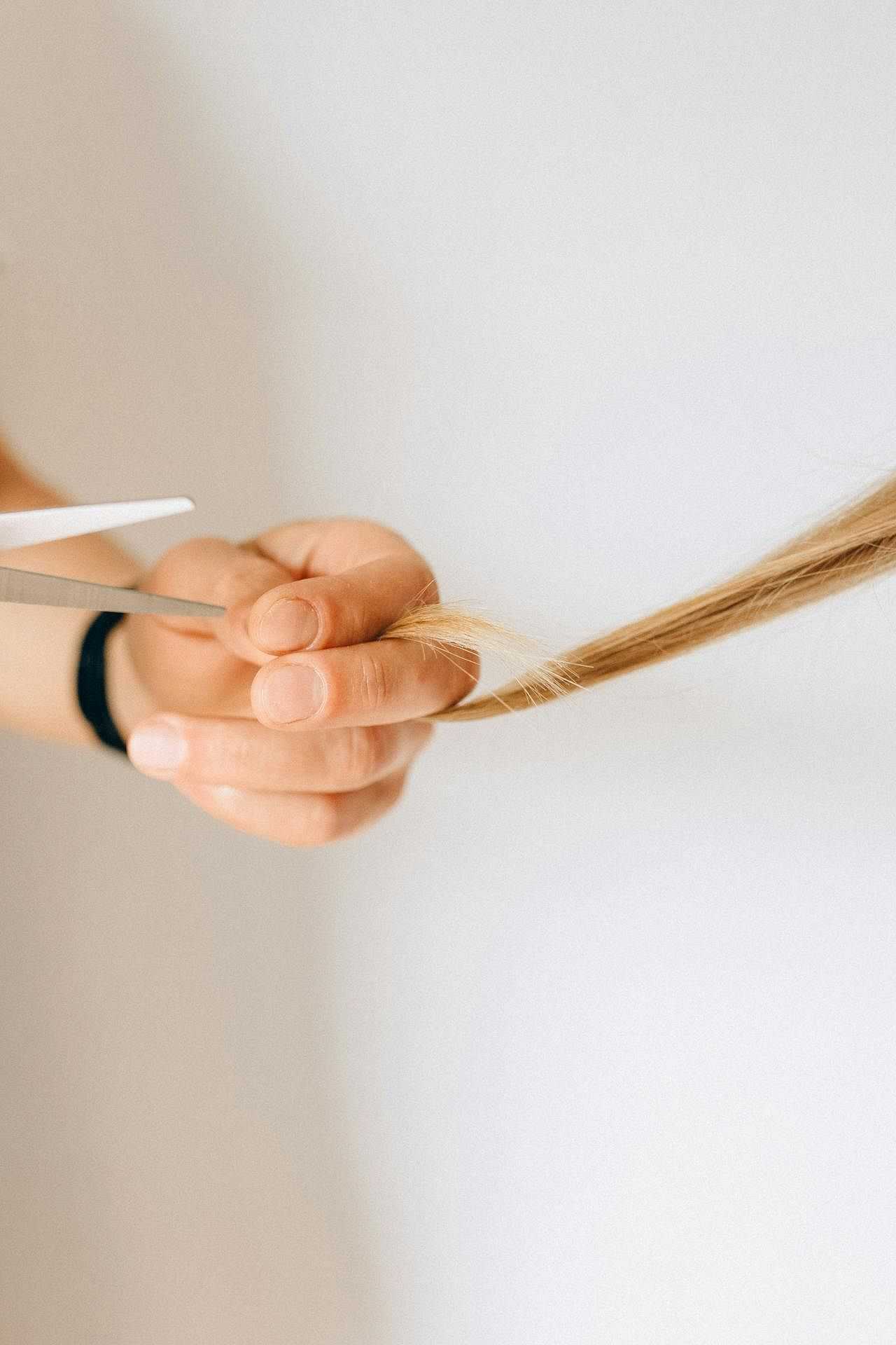 Close-up of hands cutting blonde hair with scissors.
