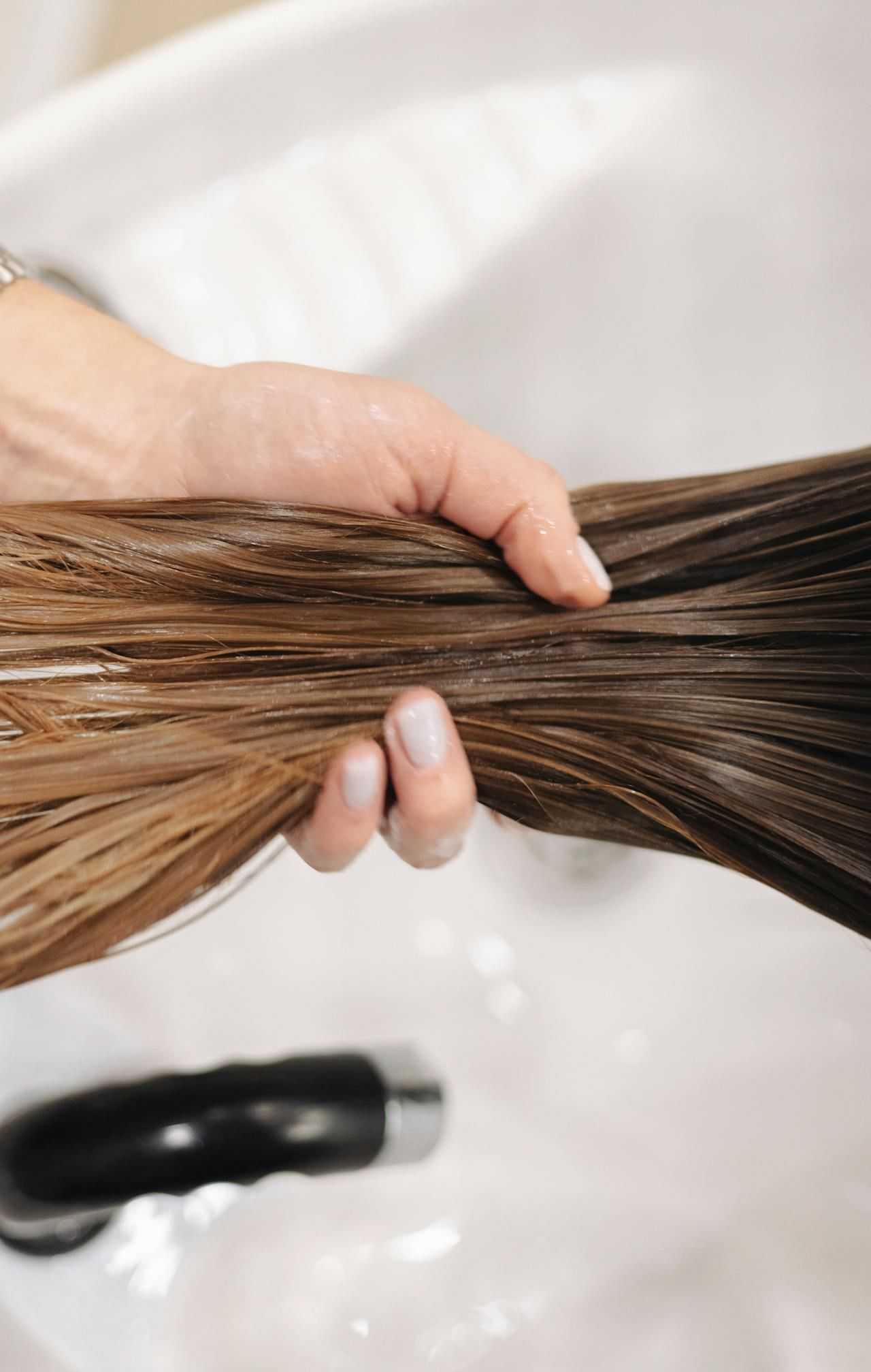 Person's hand holding wet brown hair strands over a white sink.